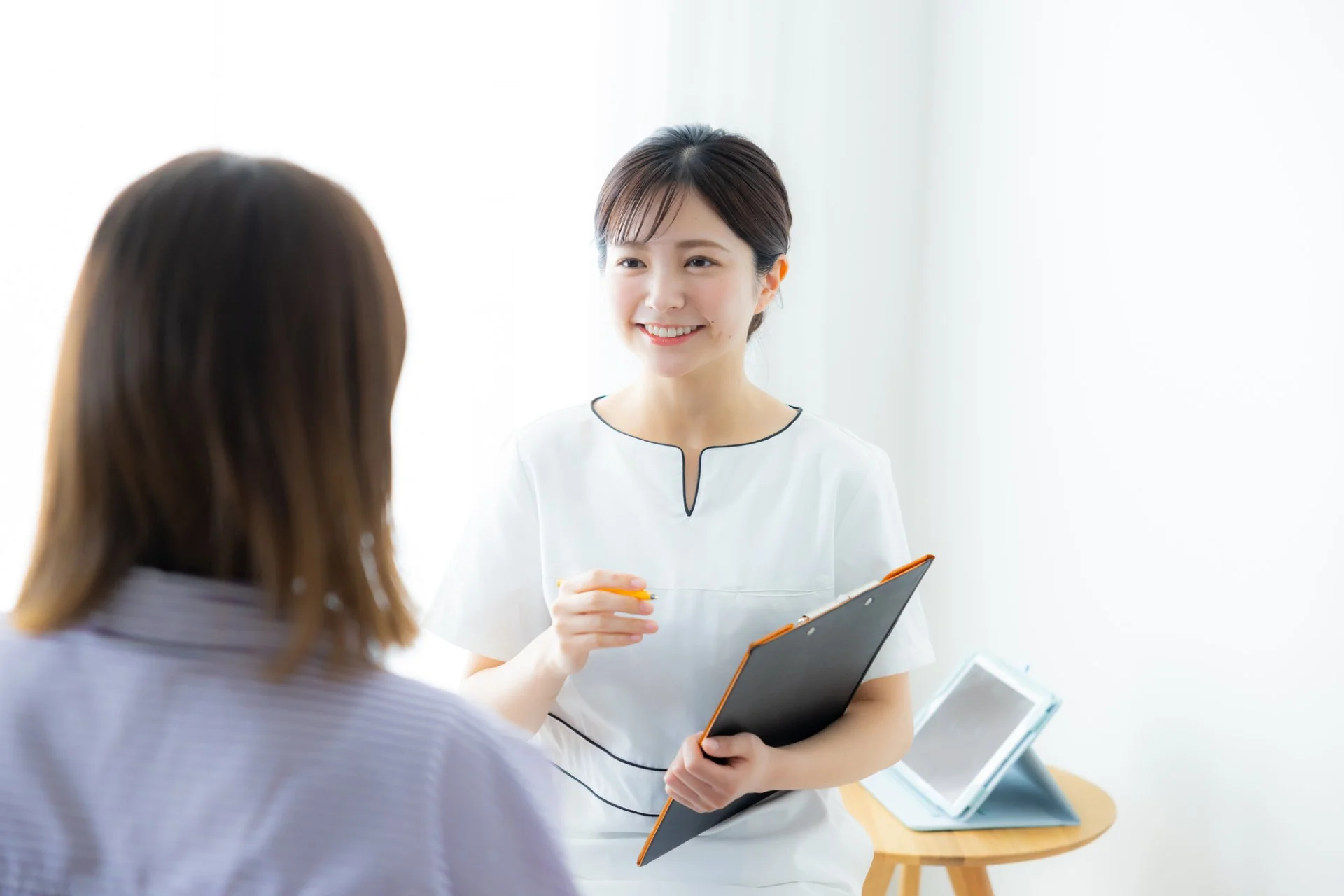 クリップボードを持ちタブレットを手にカウンセリングを行うスタッフと来店者